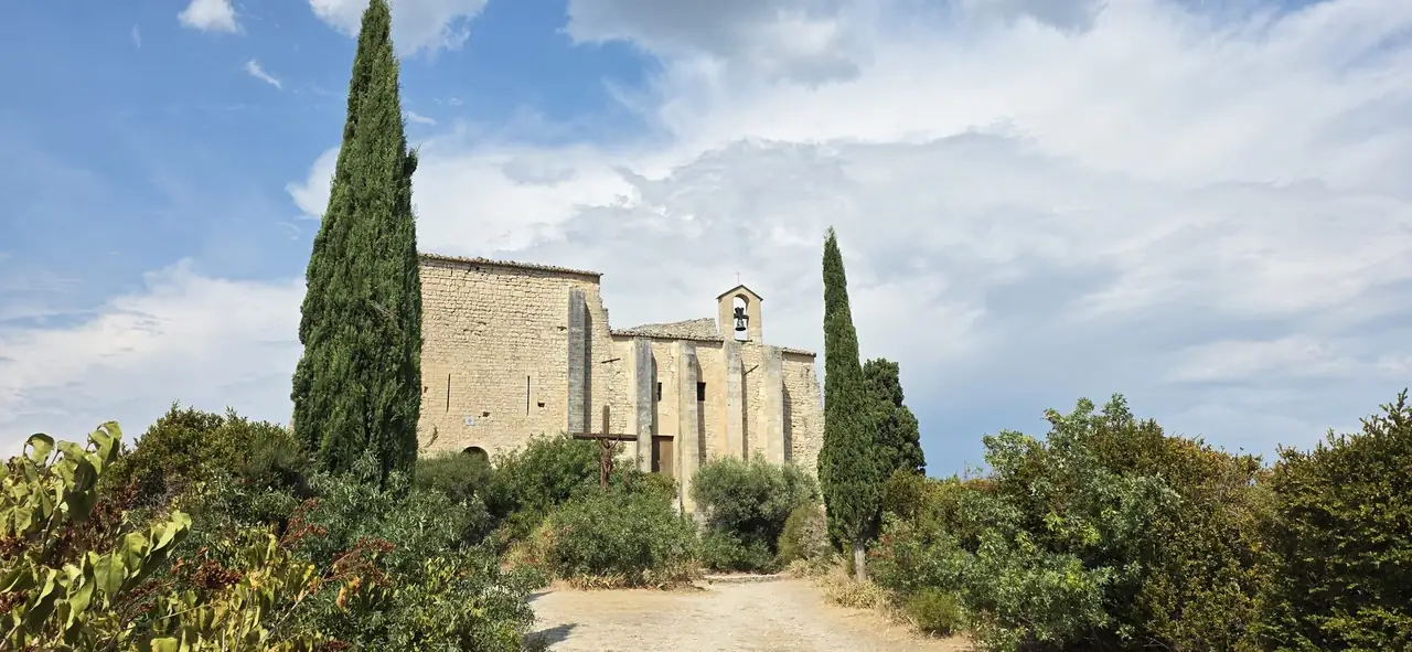 Chapelle en pierre encadrée de cyprès, sous un ciel d'été