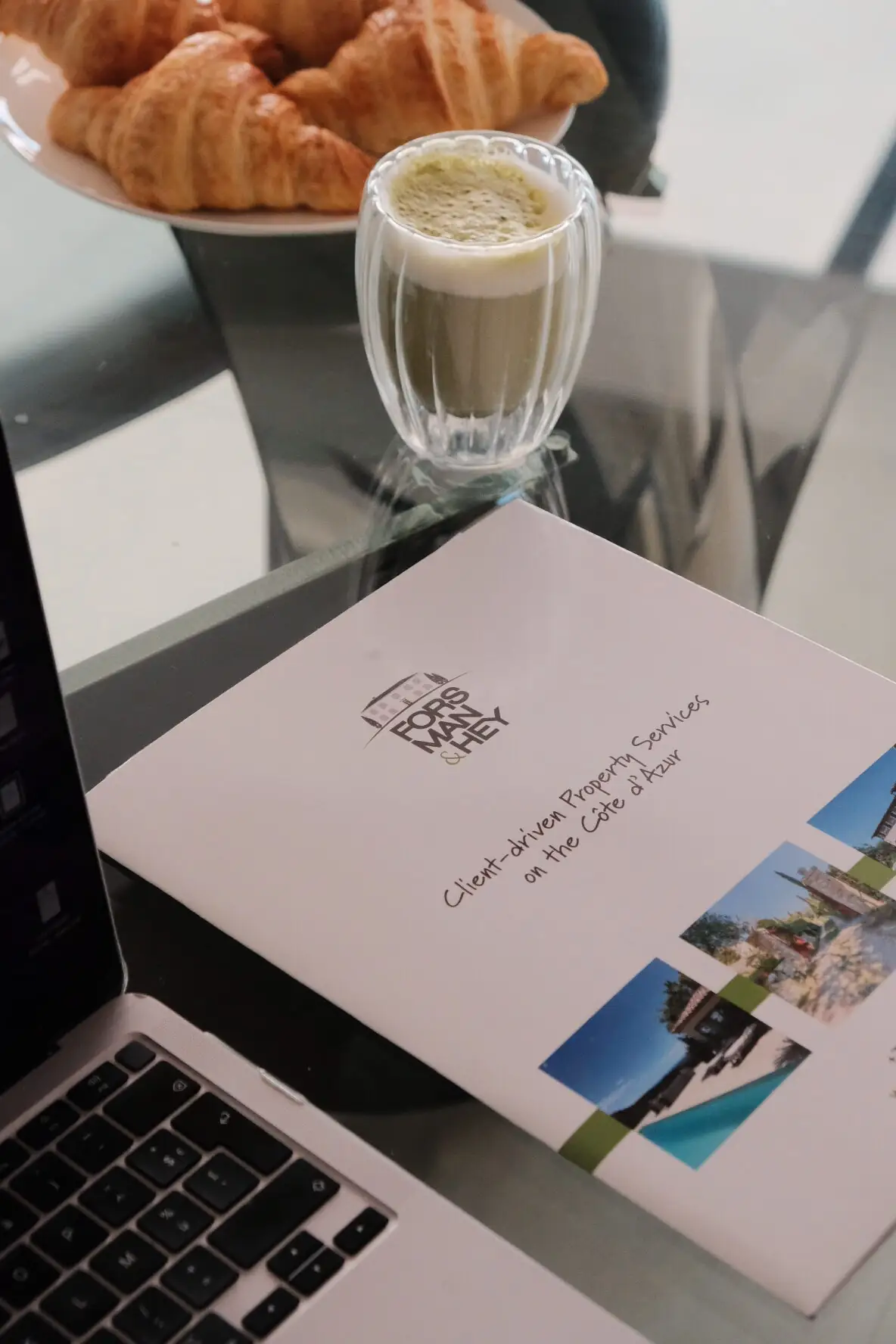 The agency brochure open on the welcome table, between a laptop and a coffee